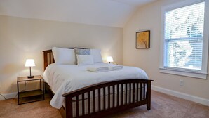 Um quarto com cama, abajures, uma janela e um quadro na parede.