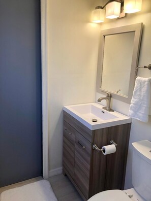 A modern bathroom with a white sink, wooden vanity, a toilet, and a mirror with lights. - Dreamy Singer Island Beach Retreat (Singer Island)