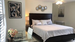A bedroom with a bed, bedside table, and a glass table with a vase of flowers. - Dreamy Singer Island Beach Retreat (Singer Island)