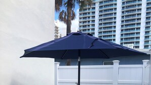 A round glass table with four chairs, a dark blue umbrella, and a white picket fence. - Dreamy Singer Island Beach Retreat (Singer Island)