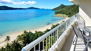 Un balcon avec vue sur une plage et une eau d’un bleu limpide.