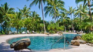 Une piscine à l’eau claire, entourée de palmiers et de chaises longues.