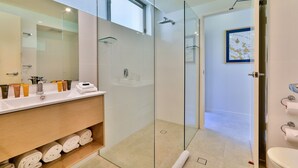 Une salle de bain moderne avec une douche à parois de verre, un lavabo blanc agrémenté d’articles de toilette et une carte encadrée accrochée au mur.