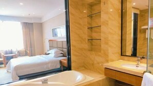 Ett hotellrum med en stor säng, ett badrum med badkar och en stor spegel.