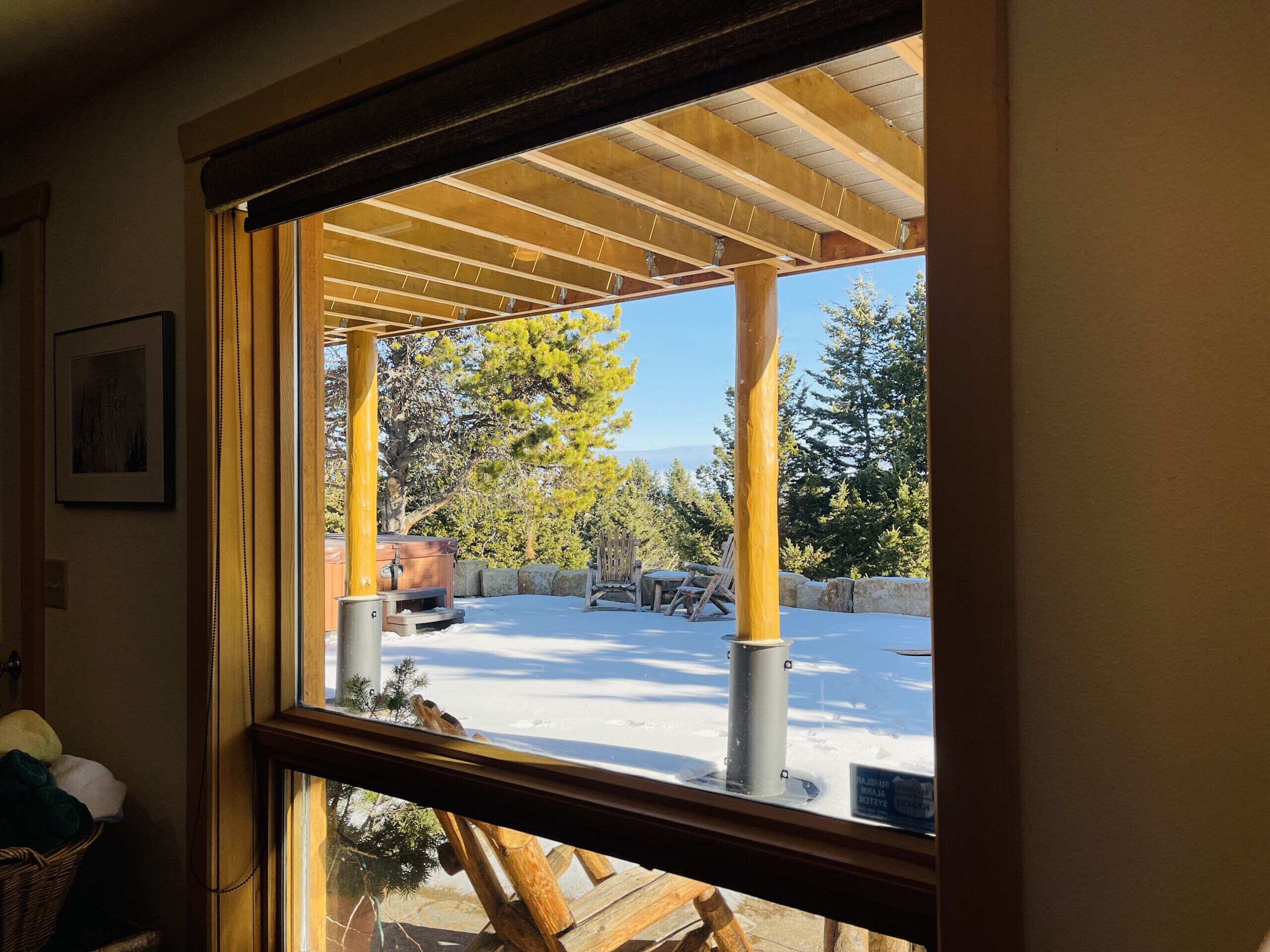 A view through a window of a covered outdoor area with a wooden ceiling, a snow-covered ground, and a wooden fence.