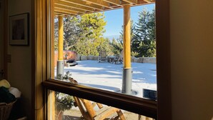 Vista a través de una ventana de un espacio al aire libre techado, con suelo cubierto de nieve y una valla de madera.