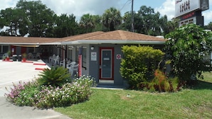 A motel with a red door, a parking lot, and a signboard. - The Scoot Inn (Port Orange)
