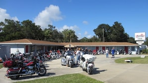 A motel with a row of parked motorcycles and a group of people standing near the entrance. - The Scoot Inn (Port Orange)