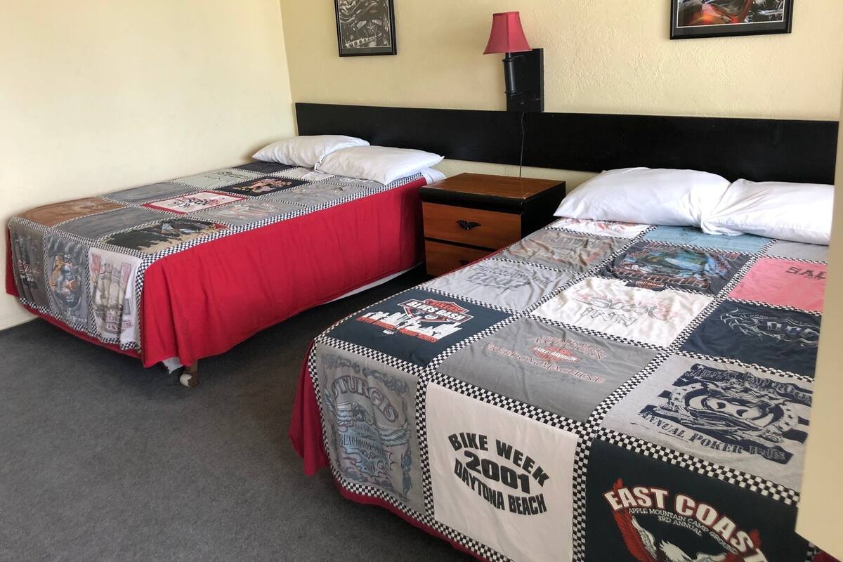 Two single beds with checkered bedding, a nightstand, a lamp, and framed pictures on the wall.