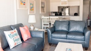 A living room with two blue leather sofas, a coffee table, and a dining area with a white table and chairs. - Cozy Condo for your family, indoor pool&Putt Putt. (Atlantic Beach)