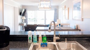 A modern kitchen with a stainless steel sink, a coffee maker, and various cleaning products on the counter. - Cozy Condo for your family, indoor pool&Putt Putt. (Atlantic Beach)