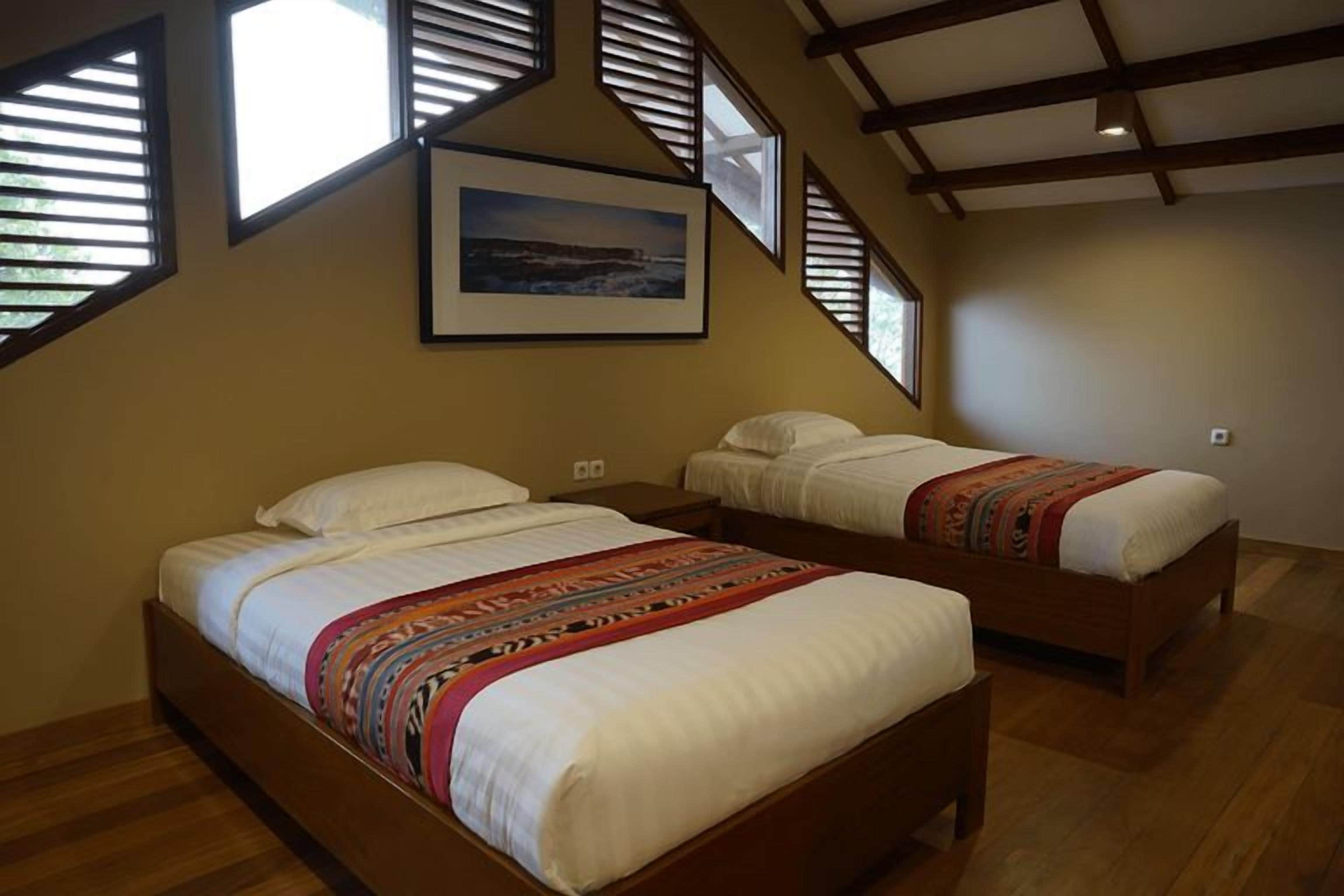 A bedroom with two beds, wooden flooring, and a sloped ceiling with skylights.
