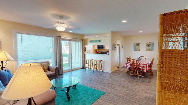 A spacious living area with a glass coffee table, a sofa, and a dining table with chairs. There is a kitchen area with a microwave and a refrigerator.