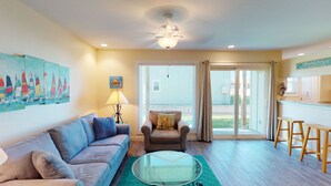 A living room with a sofa, armchair, glass coffee table, and a painting of sailboats.