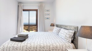 A bedroom with a large bed, a view of the sea, and a window with curtains.