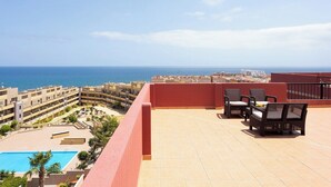 A rooftop terrace with a pool, outdoor furniture, and a view of the sea and buildings.