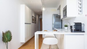 A modern kitchen with white cabinetry, a central island with stools, a coffee machine, and a hanging light fixture.