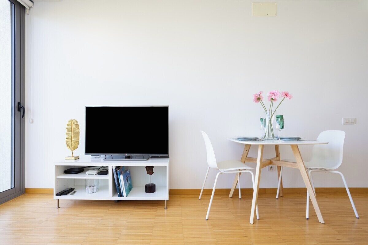 Een moderne woonkamer met een flatscreen-tv, witte meubels en een eettafel met stoelen.