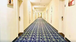 A hotel hallway with a patterned carpet, doors on both sides, and artwork on the walls. - 7 Days Inn (Dongying)