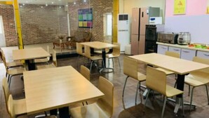 A dining area with multiple tables and chairs, a brick wall, and a kitchen area with appliances. - 7 Days Inn (Dongying)