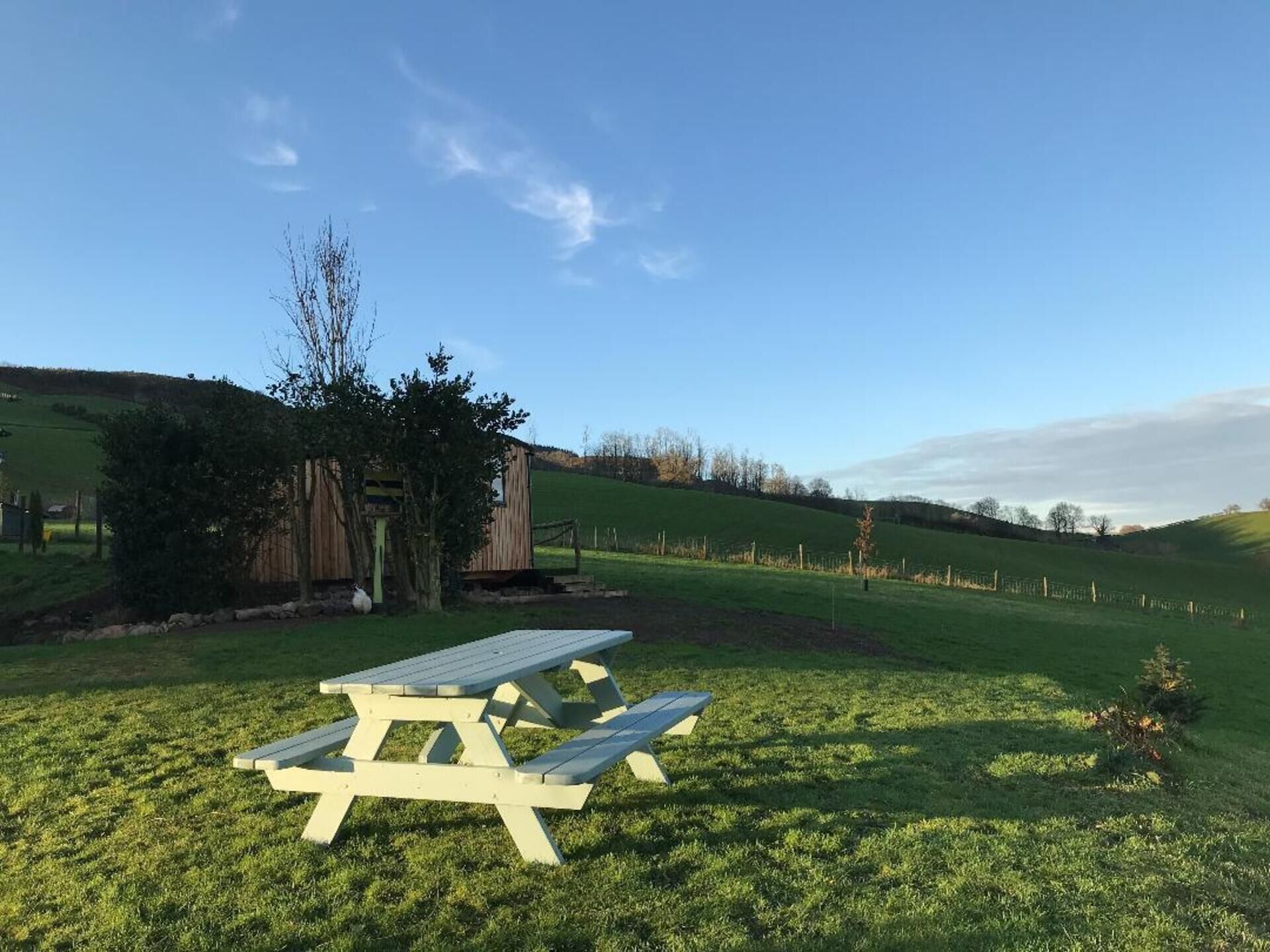 A picnic table in a grassy field with a wooden structure in the background.