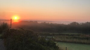 A rural landscape with a sunrise or sunset, fields, and a distant horizon.