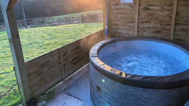 A hot tub in a wooden gazebo with a view of a grassy field.