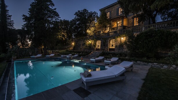 A swimming pool with lounge chairs and a stone deck, surrounded by trees and a building with illuminated windows. - Villa del Poeta - Homelike Villas (Loro Ciuffenna)