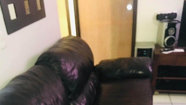 A dark brown leather sofa in a room with a tiled floor and a wooden cabinet with a speaker. - Come, Relax and feel at Home (Tijuana)