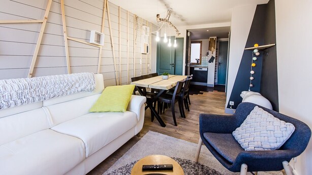Uma sala de estar moderna com um sofá branco, uma poltrona azul e uma mesa de jantar de madeira.