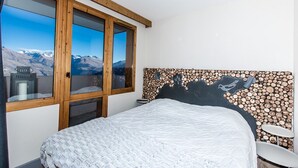 Quarto com uma cama grande, vista das montanhas pela janela e cabeceira decorada com toras.