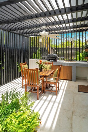 Eine Terrasse im Freien mit Holztisch und -stühlen, einem Grill und einer Pergola.