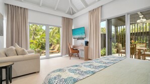 Un dormitorio amplio con una cama grande, un escritorio, una silla, un sofá y vistas a un jardín a través de puertas corredizas de vidrio.