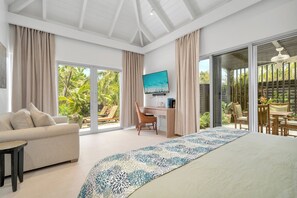 Un dormitorio amplio con una cama grande, un escritorio, una silla, un sofá y vistas a un jardín a través de puertas corredizas de vidrio.