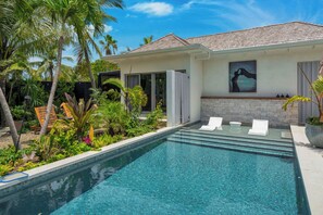 Una piscina con superficie de agua azul cristalina, rodeada de vegetación exuberante y palmeras.