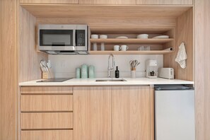 Une cuisine compacte équipée d’un four à micro-ondes encastré, d’un évier et d’un lave-vaisselle. On y trouve des placards en bois et un plan de travail sur lequel sont disposés divers ustensiles de cuisine.