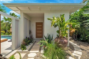 Una casa moderna con fachada blanca, puerta de madera y un jardín con diversas plantas y un camino.