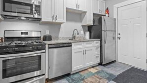 A modern kitchen with stainless steel appliances, white cabinetry, and a patterned rug. - Comfortable stay in historic Sherman Hill-3 (Des Moines)