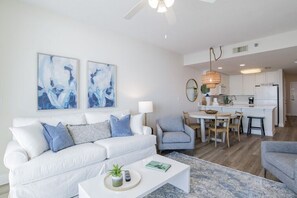 Un salon moderne avec un canapé blanc, des coussins bleus, une table basse et une œuvre d’art abstraite accrochée au mur.
