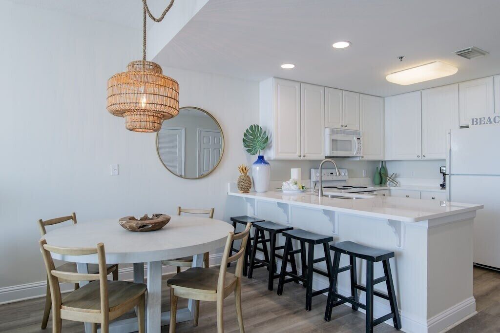 Una cocina moderna con armarios blancos, una isla central con taburetes, una lámpara colgante y un espejo redondo en la pared.
