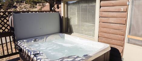 Un bain à remous situé dans un espace extérieur abrité, doté d’une terrasse en bois et d’une fenêtre avec des stores.
