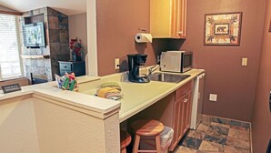 Cocina compacta con lavamanos, microondas y cafetera. Incluye un taburete pequeño y un cubo de basura.