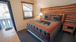 Un dormitorio con una cama que incluye un edredón con motivos de oso, un cabecero de madera, una mesita de noche y una lámpara.