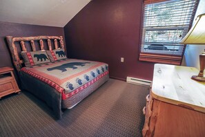 Een slaapkamer met een bed, voorzien van een sprei met een beer dessin, een houten hoofdbord en een nachtkastje.
