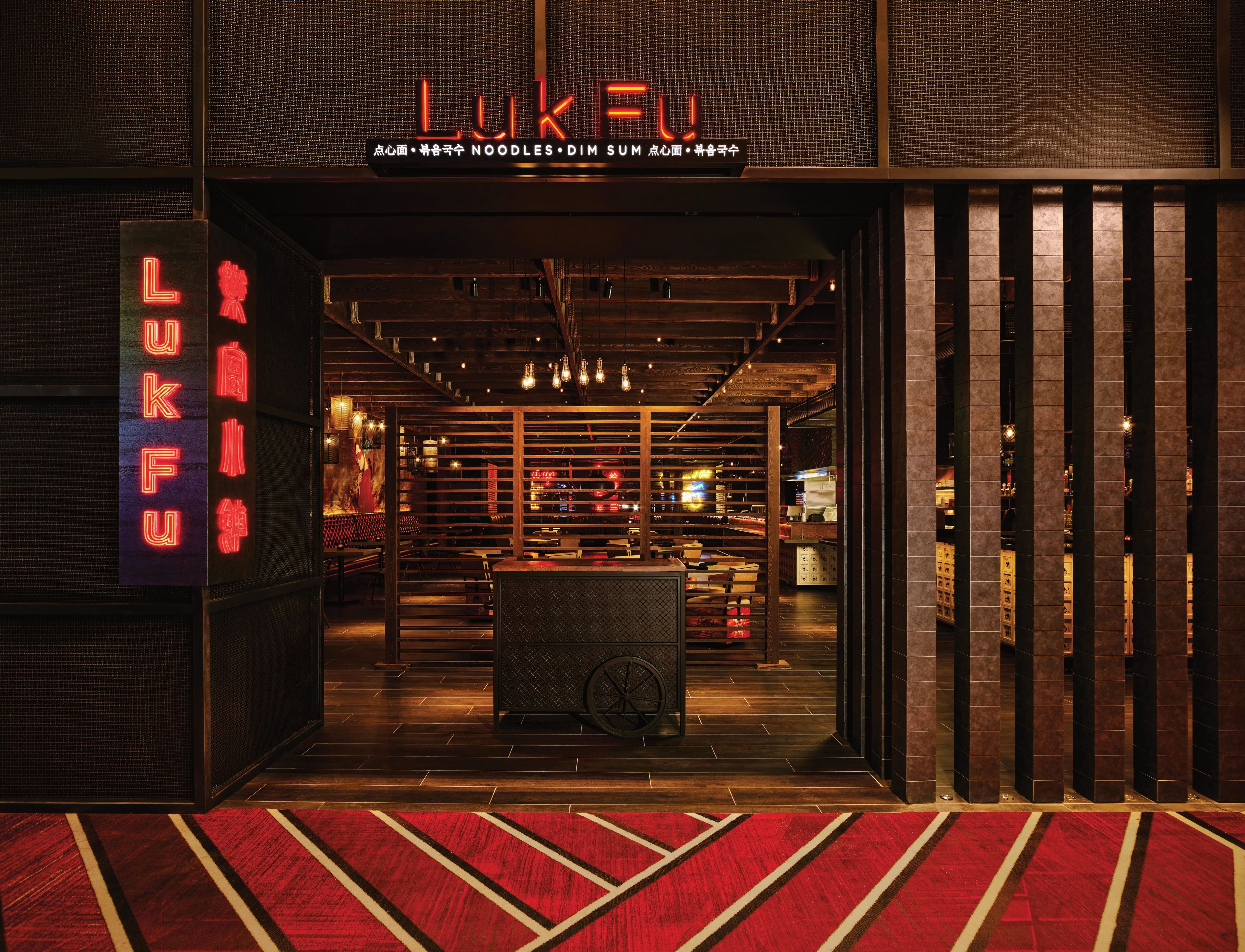 L’entrée d’un restaurant, avec une enseigne au néon, un intérieur en bois et un tapis rouge.