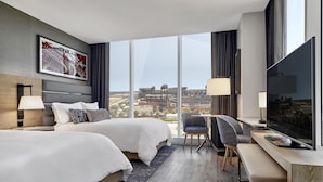Quarto de hotel moderno com duas camas, uma escrivaninha, uma cadeira e uma televisão grande.