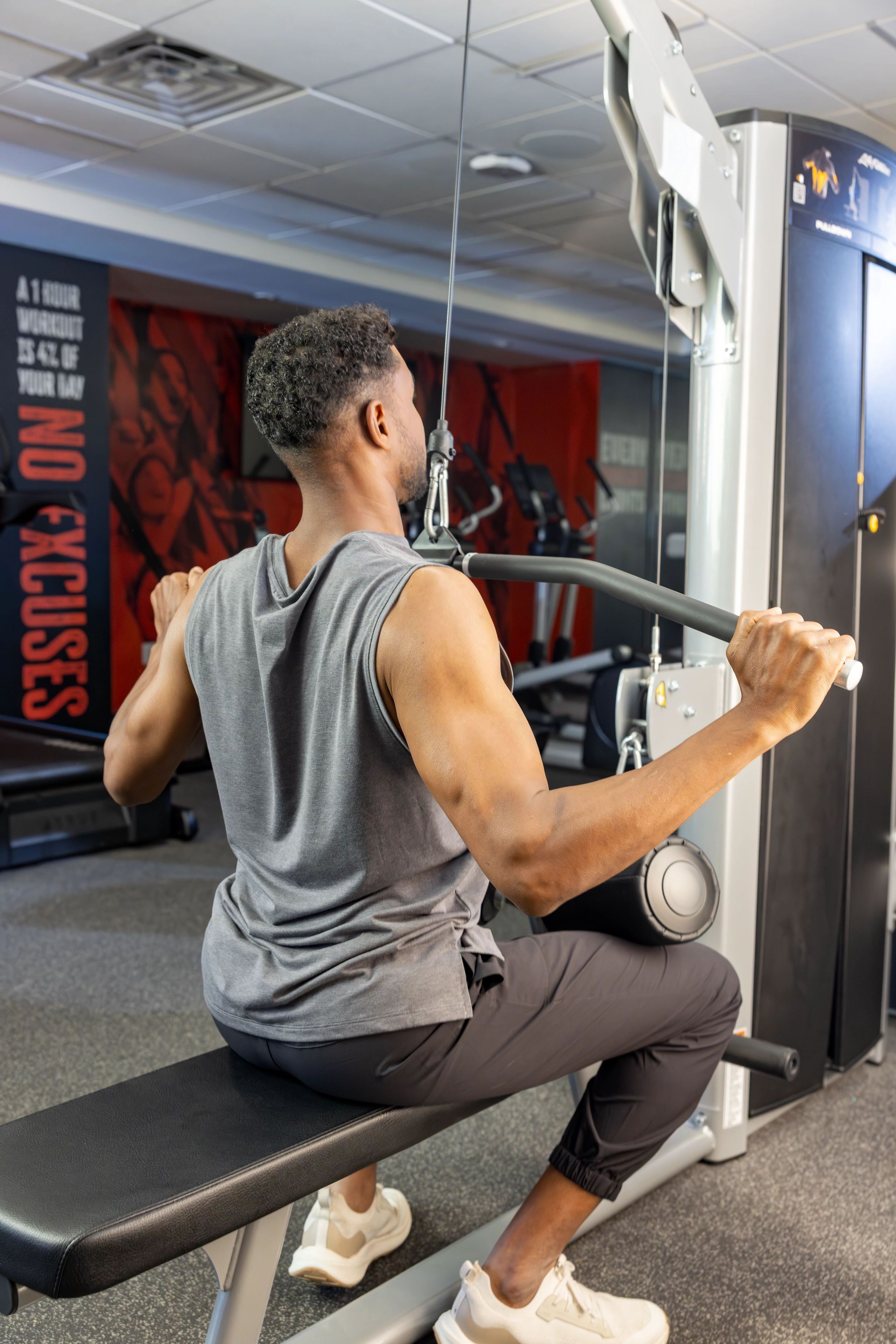 A person using a cable machine in a gym with a red wall in the background.