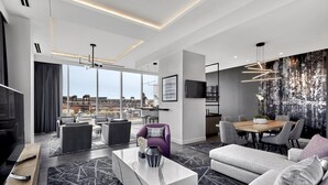 Uma sala de estar moderna com uma televisão grande, assentos confortáveis, uma área de jantar e vista para a cidade.