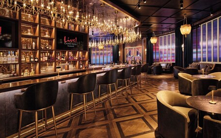 A bar area with a 'Live!' sign, a variety of liquor bottles, and a modern chandelier.