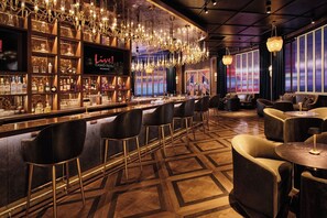 Een bar met een 'Live!' bord, diverse drankflessen en een moderne kroonluchter.